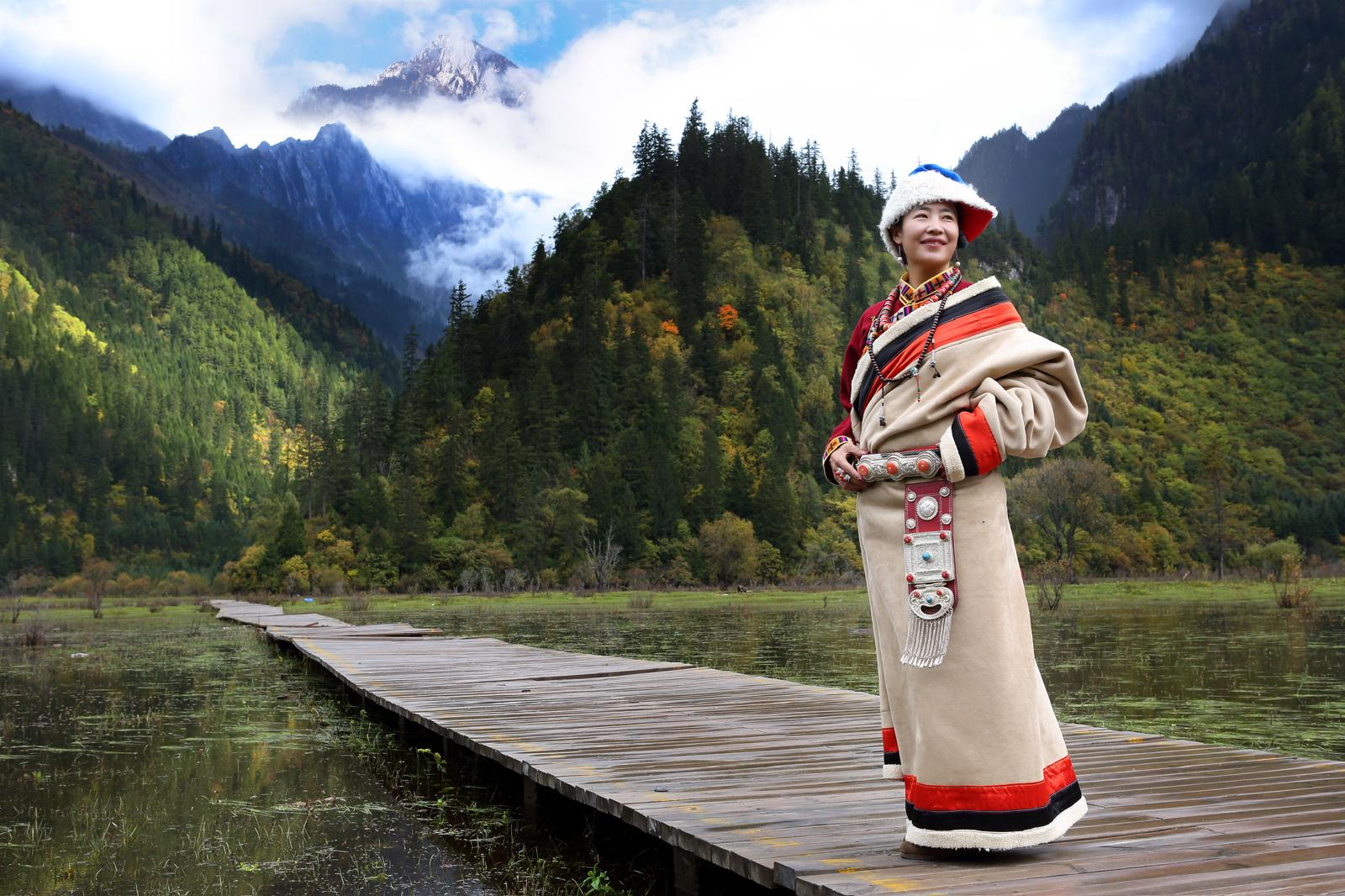 Femme en habit traditionnel tibétain sur un ponton de bois, montagnes enneigées en arrière-plan